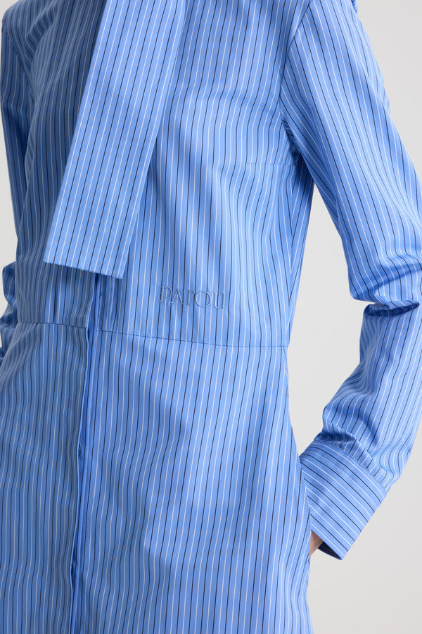 Patou - 오가닉 코튼 포플린 소재 스카프 칼라 셔츠 드레스 - Ice Blue Stripes - 아이스 블루 컬러의 오가닉 코튼 드레스. 스트라이프 패턴. 무릎 길이. 밀착된 핏에서 넓게 퍼지는 플레어 실루엣. 루프 디테일이 돋보이는 앞면의 스카프 칼라. 앞면의 히든 버튼 클로저. 허리 부분의 파투 로고 자수. 버튼 디테일의 커프스. 측면 포켓.