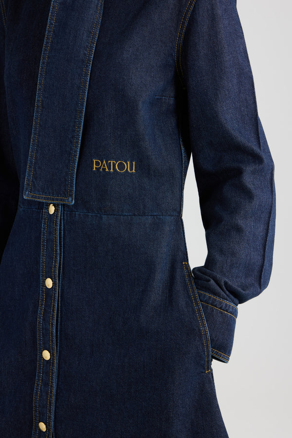 Patou - Chemisier con collo a sciarpa in denim misto cotone - Blue Moon Rodeo - Abito in denim misto cotone Blue Moon Rodeo. Motivo a righe. Lunghezza al ginocchio. Silhouette aderente e svasata. Collo a sciarpa con passante sul davanti. Chiusura sul davanti con bottone nascosto. Logo Patou ricamato in vita. Polsini abbottonati. Tasche sui lati.