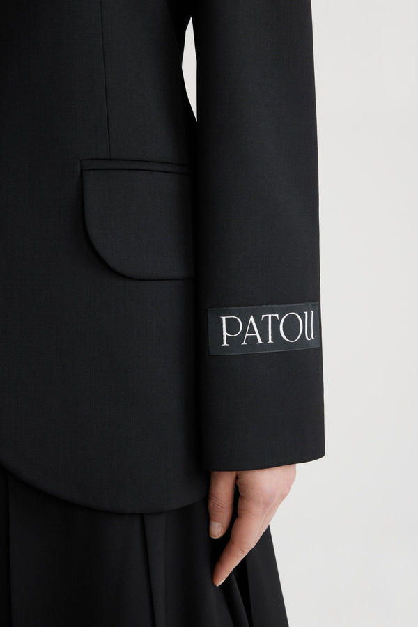 Patou - 테크니컬 울 여유로운 벨트 재킷 - Black - 블랙 컬러의 테크니컬 울 트윌 소재. 여유로운 핏. 노치 라펠. JP 인그레이빙 버튼. 버클로 사이즈 조절 가능한 탈착 가능한 벨트. 플랩 포켓. 버튼 디테일의 커프스. 왼쪽 슬리브의 Patou 라벨. 안감 처리.