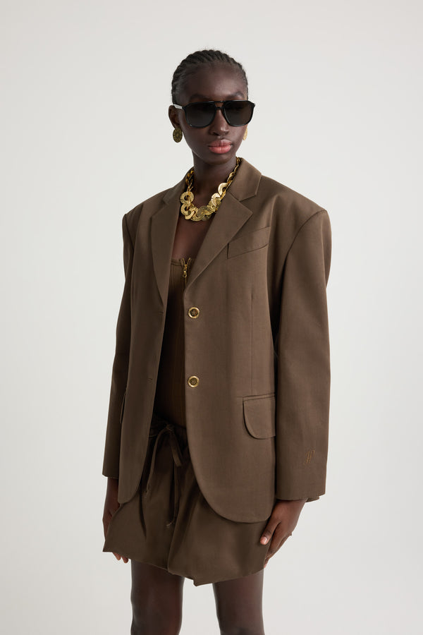 Patou - オーガニックコットンギャバジン オーバーサイズ ベルトジャケット - Java Brown - ジャバブラウンのオーガニックコットンギャバジン製ジャケット。オーバーサイズのテーラードシルエット。シングルブレストスタイル。ノッチラペル。パッド入りショルダー。ゴールドトーンのJP刻印入りボタン。チェストウェルトポケット、フラップポケット。ウエストに取り外し可能なセルフタイベルト左袖にJPモノグラム刺繍。裏地付き。