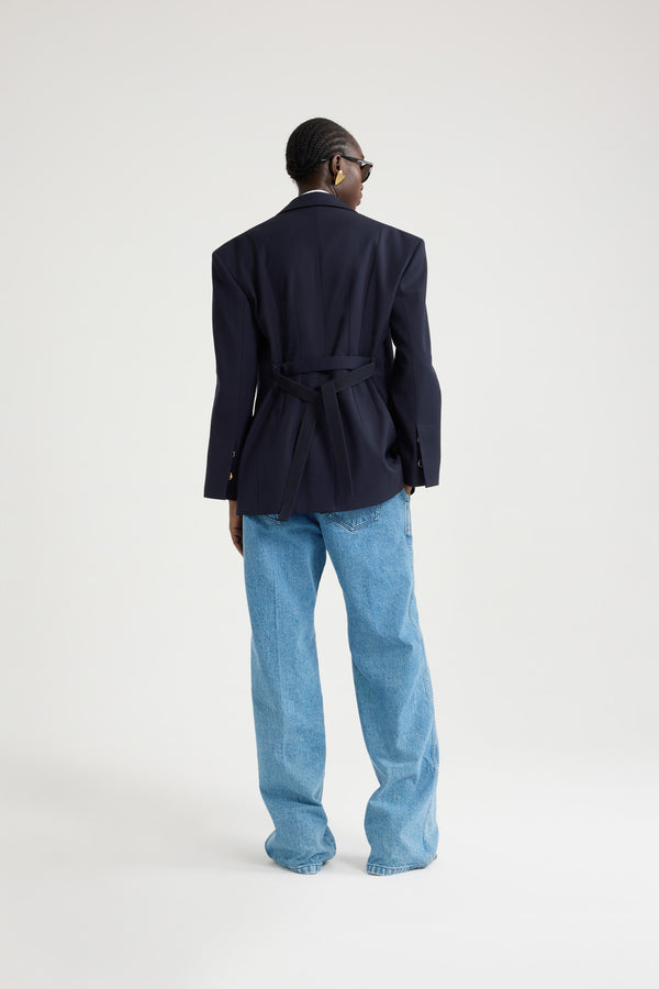 Patou - サステナブル テクニカル ウールツイル オーバーサイズ ベルテッドジャケット - Navy Black - ネイビーブラックのサステナブルなテクニカルウールツイルジャケット。オーバーサイズのテーラードシルエット。シングルブレストスタイル。ノッチラペル。パッド入りショルダー。ゴールドトーンのJP刻印入りボタン。チェストウェルトポケット、フラップポケット。ウエストに取り外し可能なセルフタイベルト左袖にJPモノグラム刺繍。裏地付き。