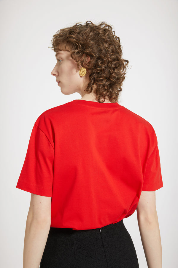 Patou - オーガニックコットン パトゥロゴTシャツ - Racing Red - パトゥを愛する人たちのデイリーアイテム。レーシングレッドのオーガニックコットン製Tシャツクルーネック、レギュラーフィット。フロント全体にパトゥロゴ。ユニセックスデザイン。 男性の方は、通常着用サイズのワンサイズ上をお選ください）。