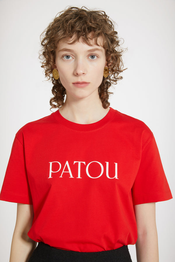 Patou - オーガニックコットン パトゥロゴTシャツ - Racing Red - パトゥを愛する人たちのデイリーアイテム。レーシングレッドのオーガニックコットン製Tシャツクルーネック、レギュラーフィット。フロント全体にパトゥロゴ。ユニセックスデザイン。 男性の方は、通常着用サイズのワンサイズ上をお選ください）。