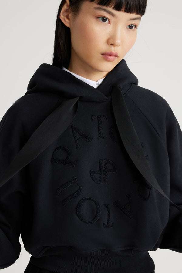 Patou - Felpa con logo medaglione in cotone bio - Black - Felpa in cotone bio nero. Vestibilità morbida. Collo con cappuccio e lacci in grosgrain. Logo Patou medaglione ricamato sul davanti. Maniche raglan. Polsini e orlo a costine.Questo modello è leggermente corto.