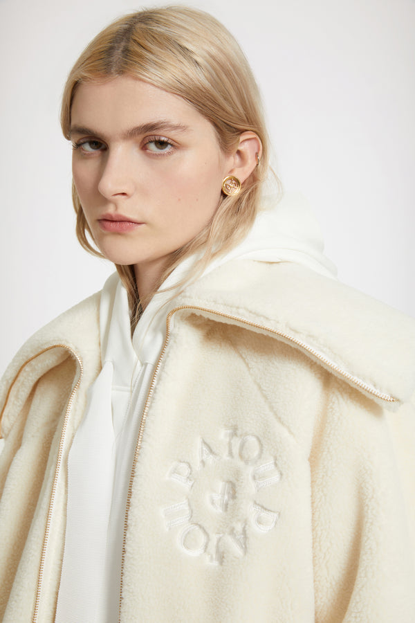 Patou - 재생 폴리에스터 소재의 인조 쉬어링 보머 재킷 - Avalanche - 순수한 쉬어링 감각.아발란체 화이트 재생 폴리에스터 보머 재킷. 인조 쉬어링 텍스처. 오버사이즈 실루엣. 과장된 디자인의 칼라. 시그니처 JP 풀탭이 달린 골드 톤 지퍼. 가슴의 파투 메달리온 로고 자수 장식. 앞면의 패치 포켓. 엘라스틱 커프스와 허리 부분.오버사이즈 스타일.