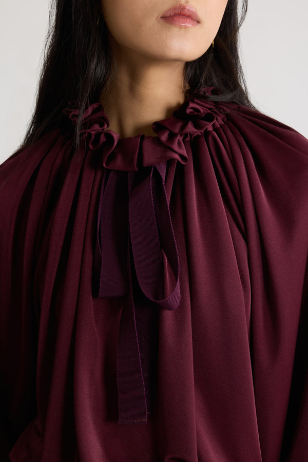 Patou - 새틴 저지 소재 아이코닉 드로우스트링 탑 - Vignola - 비뇰라 마룬 컬러의 새틴 저지 탑. 앞면의 플라운스 주름을 넣은 드로우스트링 칼라, 긴 그로그랭 타이. 신축성 있는 커프스의 배트윙 슬리브. 신축성 있는 허리 부분.