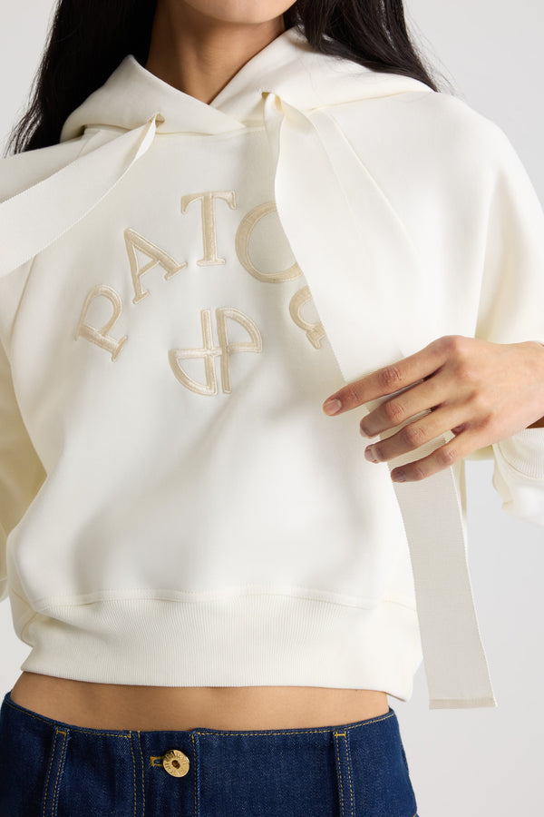 Patou - オーガニックコットン パトゥロゴ＆JPモノグラム フーディ - Snowberry White - スノーベリーホワイトのオーガニックコットン製スウェットシャツ。クロップド丈。フード付き襟にグログラン ドローストリング。前面にパトゥの刺しゅうロゴとJPモノグラム。ラグランスリーブ。リブ編みの袖口と裾。