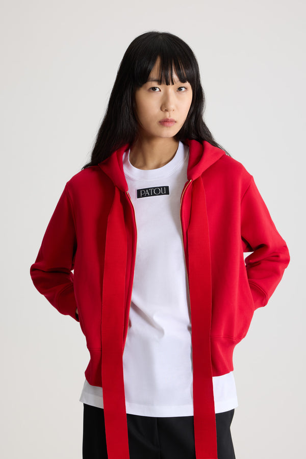 Patou - オーガニックコットンフリース パトゥロゴ＆JPモノグラム ジップアップフーディ - Scarlet Red - スカーレットレッドのオーガニックコットンフリース製フーディー。フード付き襟にグログラン ドローストリング。前面にゴールドトーンのファスナー。バックにパトゥの刺しゅうロゴとJPモノグラム。サイドポケット付き。リブ編みの袖口と裾。