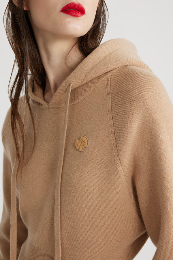 Patou - サステナブルウール＆カシミアブレンド フーディー - Biscuit - ビスケットベージュのサステナブル ウール＆カシミア混紡セーター。リラックスフィット。ドローストリング付きフーディーカラー。ラグランスリーブ。チェストにJPブークレパッチ。リブ編みの袖口と裾。フィット感のあるウエスト。