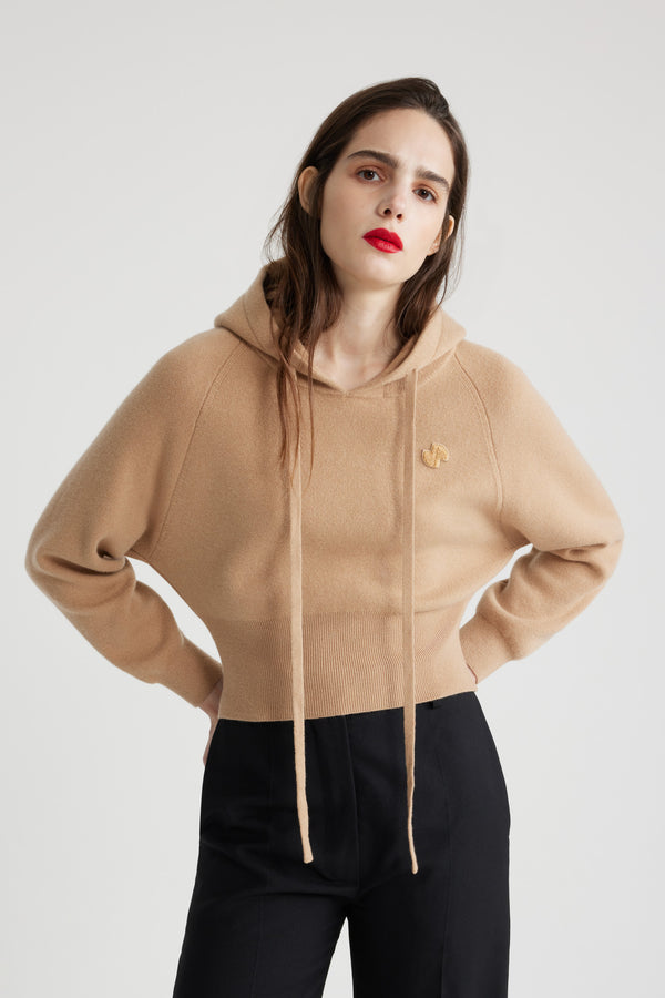 Patou - サステナブルウール＆カシミアブレンド フーディー - Biscuit - ビスケットベージュのサステナブル ウール＆カシミア混紡セーター。リラックスフィット。ドローストリング付きフーディーカラー。ラグランスリーブ。チェストにJPブークレパッチ。リブ編みの袖口と裾。フィット感のあるウエスト。