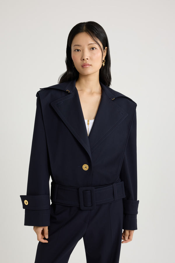 Patou - サステナブル テクニカル ウールツイル ベルテッドジャケット - Navy Black - ネイビーブラックのサステナブルなテクニカルウールツイルジャケット。ルーズフィット。ワイドカラー。ボタン付きのショルダー＆カフスタブ。前面にボタン開閉。ゴールドトーンのパトゥロゴ刻印入りボタン。ウエストに幅広の布製ベルト。サイドにポケット。トップステッチ ディテール。裏地付き。