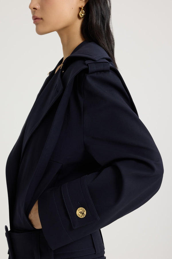 Patou - サステナブル テクニカル ウールツイル ベルテッドジャケット - Navy Black - ネイビーブラックのサステナブルなテクニカルウールツイルジャケット。ルーズフィット。ワイドカラー。ボタン付きのショルダー＆カフスタブ。前面にボタン開閉。ゴールドトーンのパトゥロゴ刻印入りボタン。ウエストに幅広の布製ベルト。サイドにポケット。トップステッチ ディテール。裏地付き。