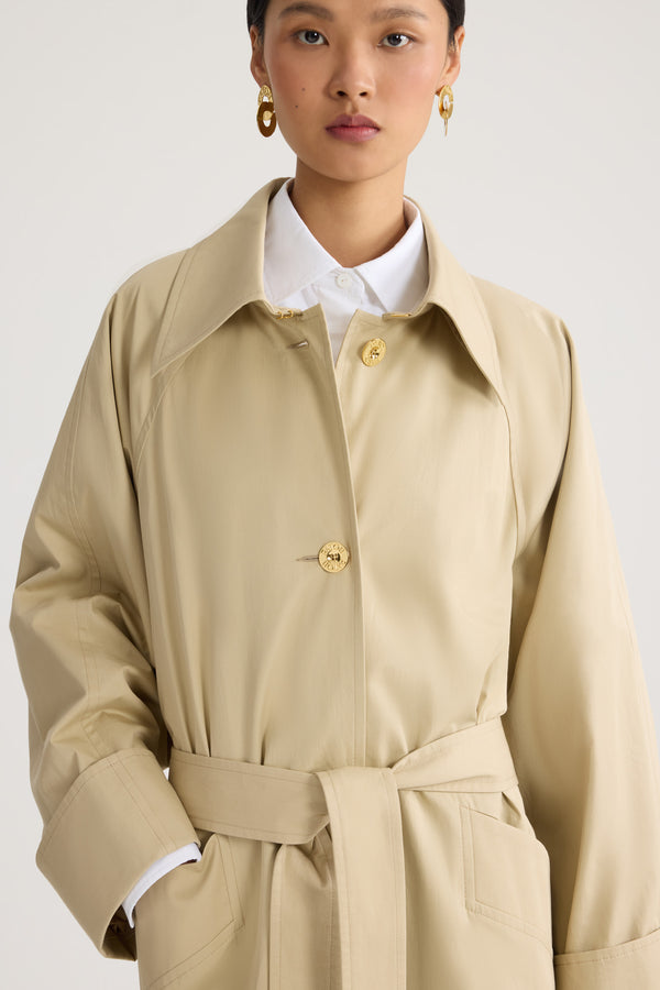 Patou - Trench-coat léger en coton bio - Safari Sand - Trench-coat léger couleur sable. Ceinture amovible à la taille. Double boutonnage doré.