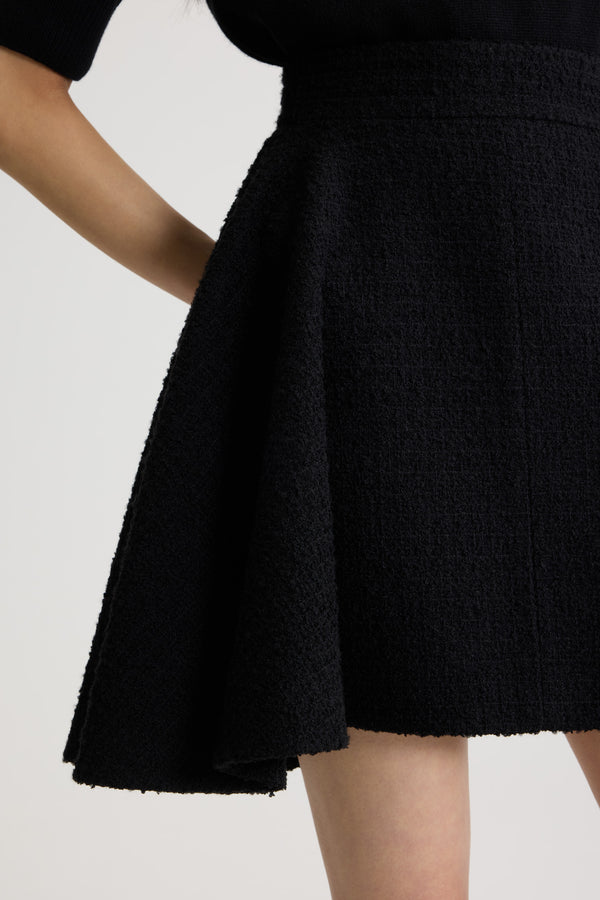 Patou - Asymmetric mini skirt in sustainable wool blend tweed - Black - Black sustainable wool blend tweed skirt. Short length. Mid waist. Asymmetric silhouette with pleating on one side. Zip fastening at the back. Single rounded pocket at the side. Lined.