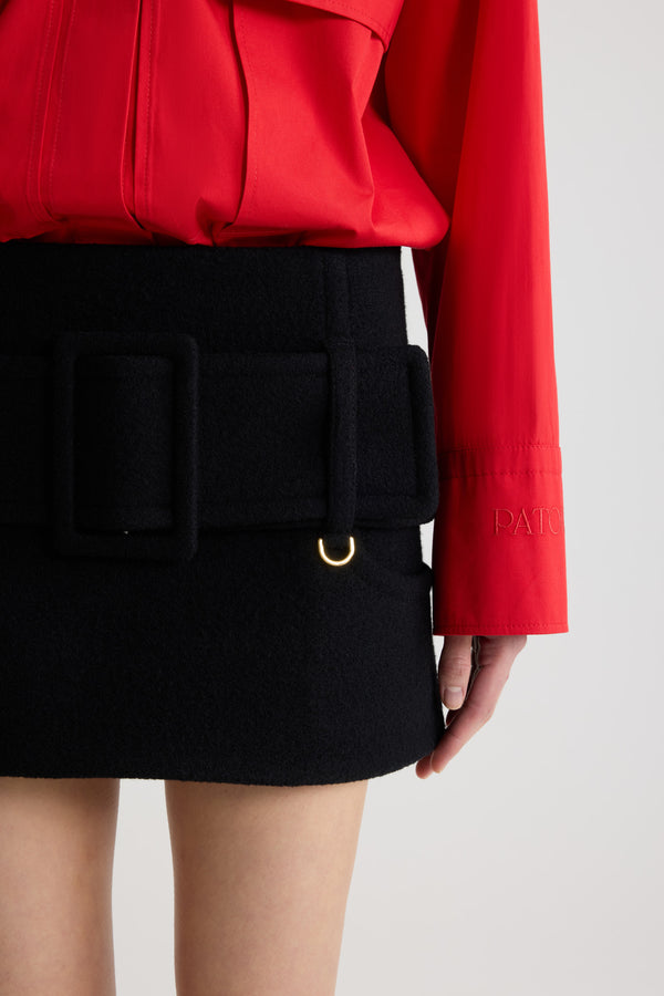 Patou - Belted mini skirt in boiled wool - Black - Black boiled virgin wool skirt. Short length. Low waist. Zip fastening at the back. Wide fabric belt at the hips with fabric-covered buckle and gold-tone D-ring. Low pockets at the front. Lined.