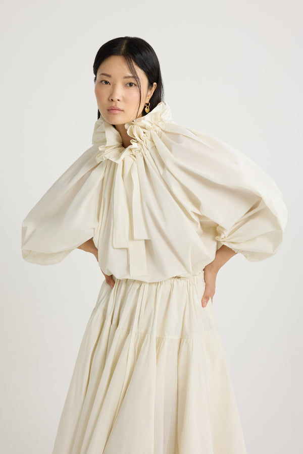 Patou - Haut à manches bouffantes en faille recyclée - Ivory - Haut en faille recyclée ivoire. Silhouette volumineuse. Col à coulisse avec détail de fronce et gros-grain. Manches chauve-souris resserrées aux poignets. Taille élastiquée.Ce top fait partie de la collection Cérémonie créée pour les occasions spéciales.