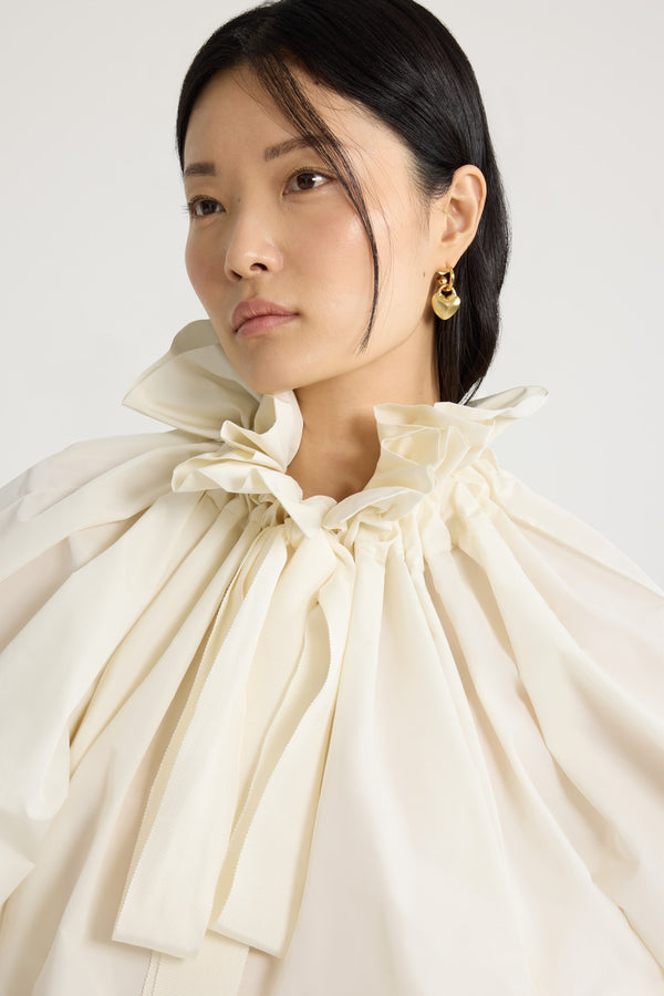 Patou - Haut à manches bouffantes en faille recyclée - Ivory - Haut en faille recyclée ivoire. Silhouette volumineuse. Col à coulisse avec détail de fronce et gros-grain. Manches chauve-souris resserrées aux poignets. Taille élastiquée.Ce top fait partie de la collection Cérémonie créée pour les occasions spéciales.