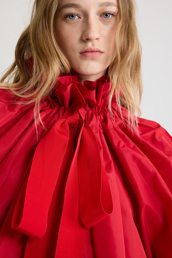 Patou - La Patou Blouse リサイクルファイユ - Lipstick Red - リップスティックレッドのリサイクルポリエステルファイユ製トップス。ネックで結んでもオフショルダーでも着用可能なハイボリューム シルエット。フロントにフラウンスをあしらったドローストリングカラー、ロンググログランタイ付き。袖口に伸縮性があるバットウィングスリーブ。伸縮性があるウエスト。