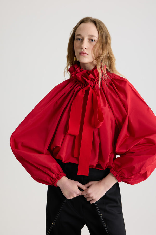 Patou - La Patou Blouse リサイクルファイユ - Lipstick Red - リップスティックレッドのリサイクルポリエステルファイユ製トップス。ネックで結んでもオフショルダーでも着用可能なハイボリューム シルエット。フロントにフラウンスをあしらったドローストリングカラー、ロンググログランタイ付き。袖口に伸縮性があるバットウィングスリーブ。伸縮性があるウエスト。