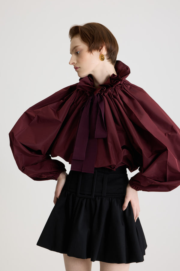 Patou - La Patou Blouse リサイクルファイユ - Vignola - ヴィニョーラマルーンのリサイクルポリエステルファイユ製トップス。ネックで結んでもオフショルダーでも着用可能なハイボリューム シルエット。フロントにフラウンスをあしらったドローストリングカラー、ロンググログランタイ付き。袖口に伸縮性があるバットウィングスリーブ。伸縮性があるウエスト。