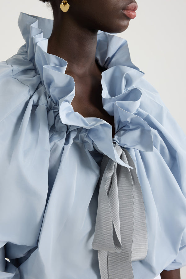 Patou - Iconic drawstring top in recycled faille - Pearl Blue - Pearl Blue recycled polyester faille top. High volume silhouette that can be worn knotted at the neck or off the shoulders. Drawstring collar with flounce at the front and long grosgrain ties. Batwing sleeves with elasticated cuffs. Elasticated waist.