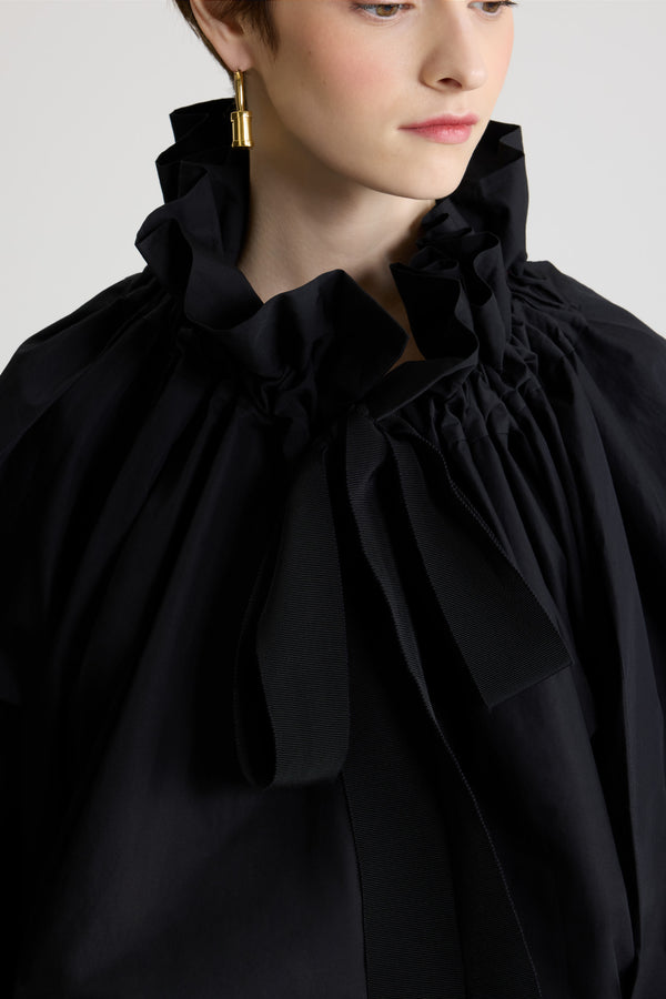 Patou - La Patou Blouse オーガニックコットンポプリン - Black - ブラックのオーガニックコットン製トップ。ネックで結んでもエンボス オフショルダーでも着用可能なハイボリューム シルエット。フロントにフラウンスをあしらったドローストリングカラー、ロンググログランタイ付き。袖口に伸縮性があるバットウィングスリーブ。伸縮性があるウエスト。
