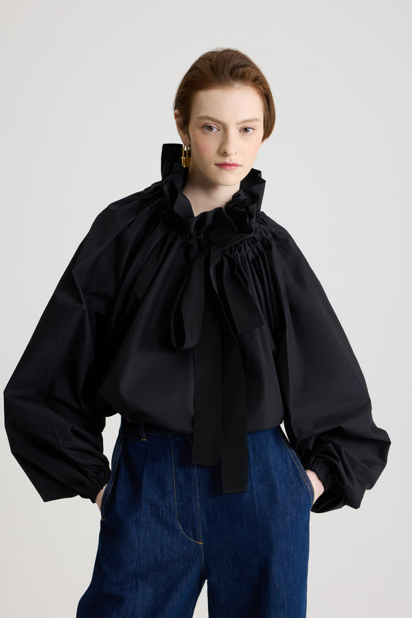 Patou - La Patou Blouse オーガニックコットンポプリン - Black - ブラックのオーガニックコットン製トップ。ネックで結んでもエンボス オフショルダーでも着用可能なハイボリューム シルエット。フロントにフラウンスをあしらったドローストリングカラー、ロンググログランタイ付き。袖口に伸縮性があるバットウィングスリーブ。伸縮性があるウエスト。