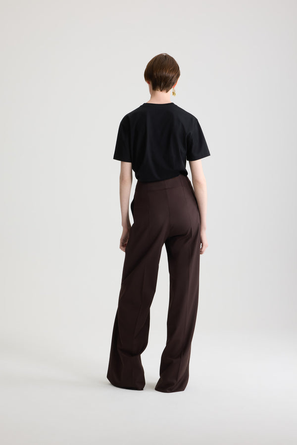Patou - サステナブルテクニカルウール フレア テーラードパンツ - Smoked Ebony - スモークドエボニーのサステナブルなテクニカルウールツイルパンツ。長めのフレアレッグ。フロントにゴールドトーンのJPモノグラム刻印入りボタンと隠しファスナー。ベルトループ付き。サイドにポケット。前面と背面にステッチクリース。