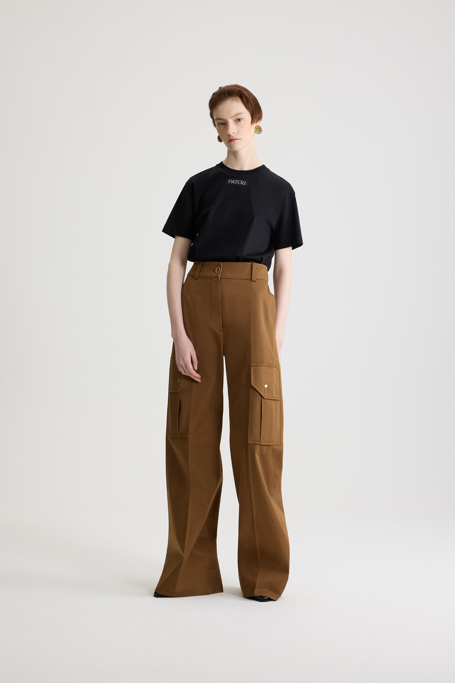 Patou - Pantalone cargo svasato in gabardine di cotone bio - Nutmeg - Pantalone in gabardine di cotone bio marrone chiaro Nutmeg. Gamba lunga svasata. Bottone oro inciso con monogramma JP e zip nascosta sul davanti. Passanti per cintura. Tasche sui lati; tasche cargo sulle gambe con bottoni a pressione oro incisi con monogramma JP. Piega cucita sul davanti e sul retro.