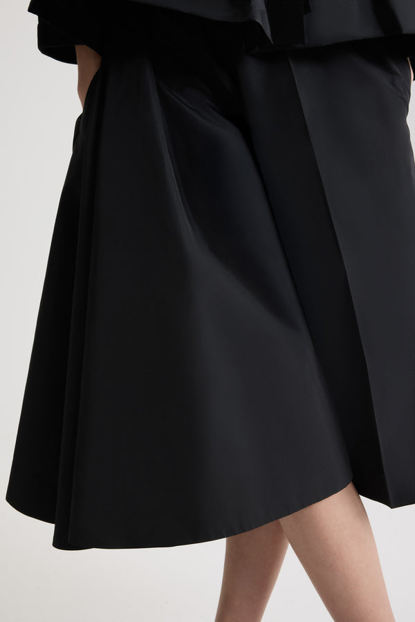 Patou - Asymmetric bermuda shorts in recycled faille - Black - Black recycled polyester faille shorts. Knee length. Mid waist. Asymmetric silhouette with pleating on one side. Elasticated waist. Pressed crease at the front and back.