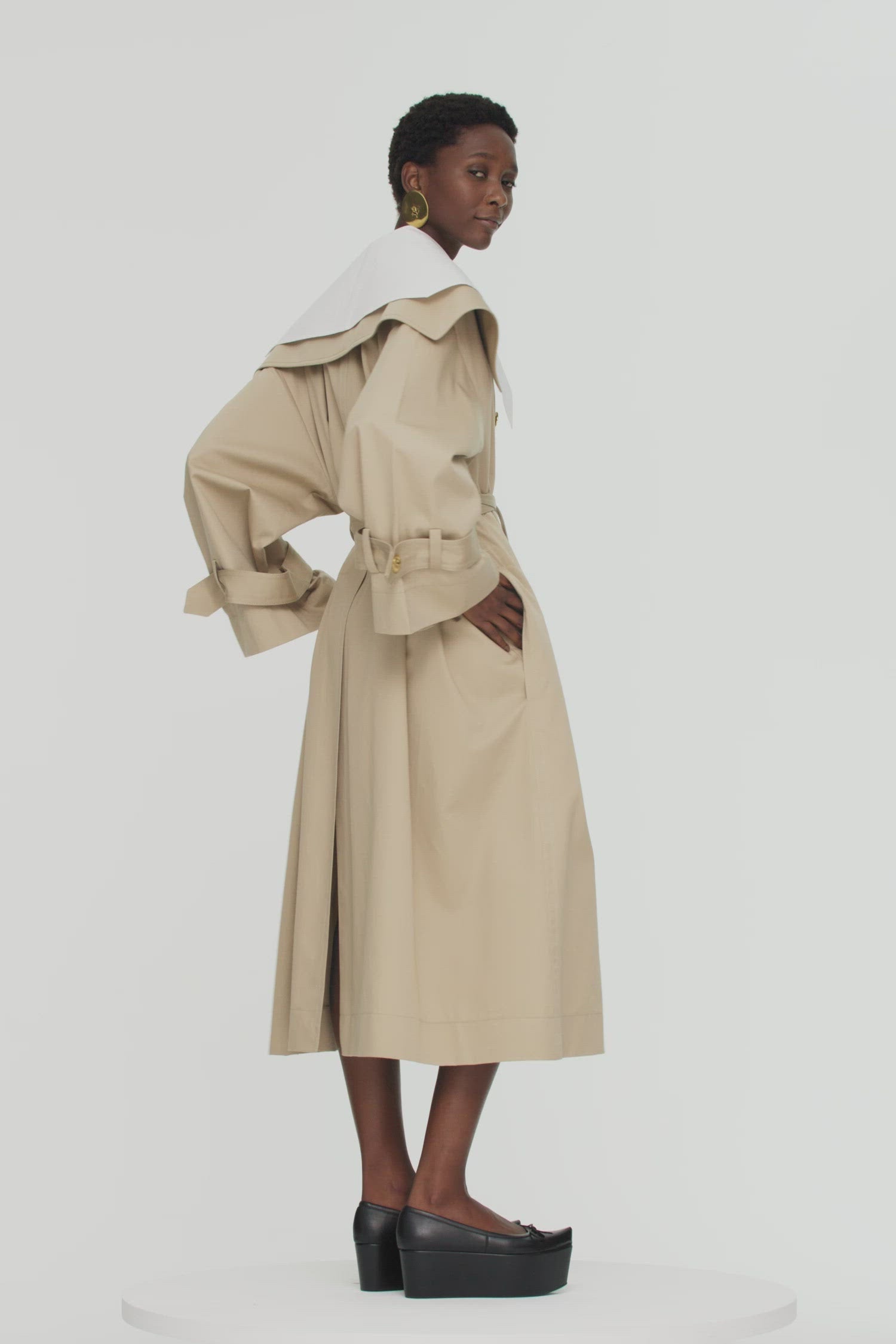 Patou - Signature trenchcoat in organic cotton - Sand - A flared trench with French flair.Signature Patou trenchcoat in Sand beige organic cotton gabardine. Double-breasted style with a slight A-line silhouette. Oversized collar and storm flap. Gold-coloured buttons with engraved Patou logo. Removable belt at the waist. Ties at the cuffs with black embroidered Patou label. Two pockets at the sides. Fully lined. Oversize fit.