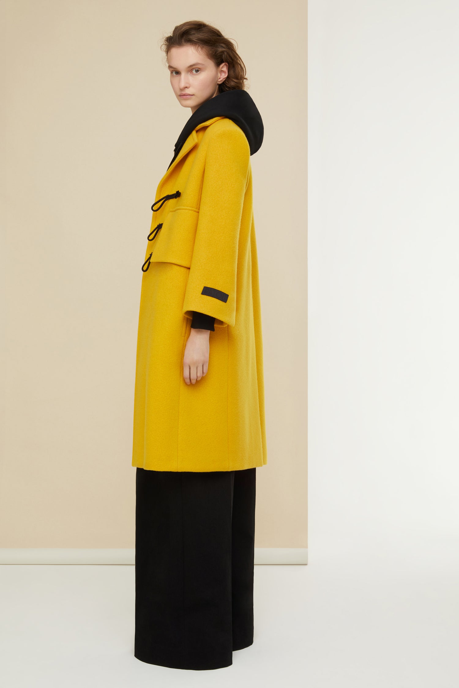 Patou - Manteau appeau en laine et cachemire recyclés - Saffron - L’appeau s’invite sur le manteau.Manteau en mélange laine et cachemire jaune safran. Silhouette longue et légèrement évasée. Fermeture par boutons en bois de style appeau ainsi que par des pressions cachées. Deux grandes fausses poches à rabat ; deux poches sur les côtés. Étiquette Patou brodée sur la manche gauche.