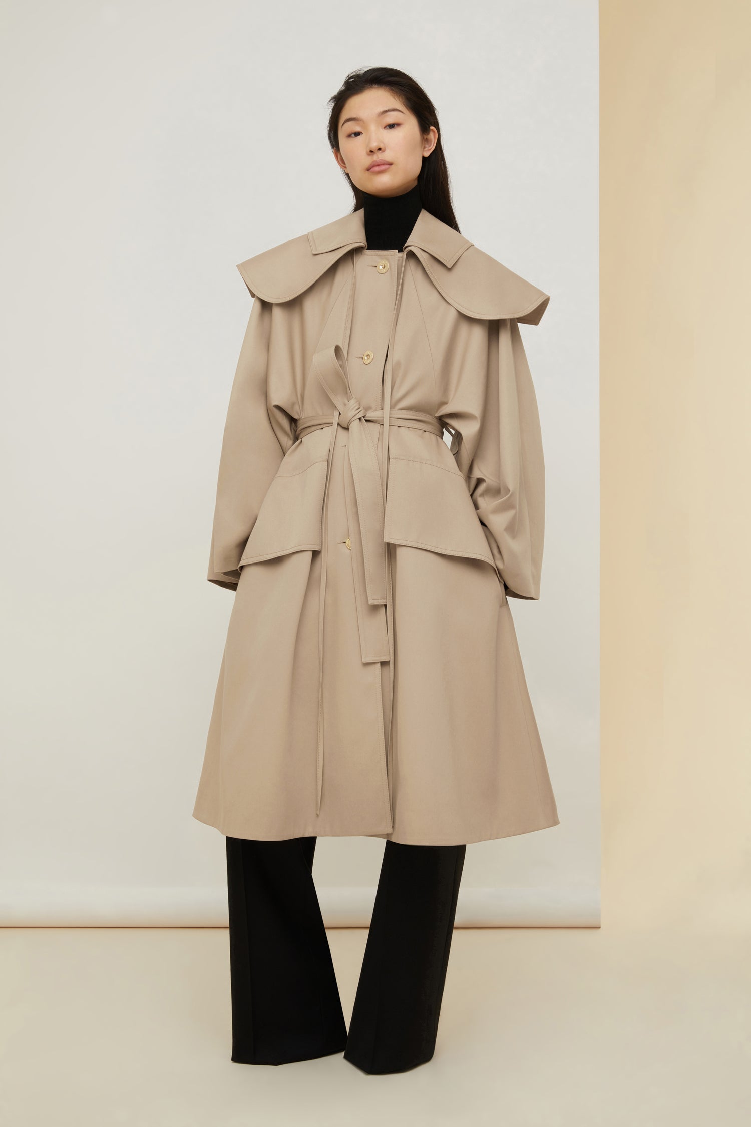 Patou - Oversize-Mantel aus Bio-Gabardine mit Gürtel und abnehmbarem Kragen - Sand - Doppelter Kragen, doppeltes Vergnügen.   Sandbeigefarbener Mantel aus Bio-Baumwoll-Gabardine. Ausgestellte Oversize-Form. Doppelter Kragen im Matrosenstil mit schwarzem Patou-Label hinten; der breitere Kragen ist abnehmbar und kann vorne gebunden werden. Weite Raglan-Ärmel. Goldfarbene Knöpfe mit Patou Logo-Gravur. Taillengürtel aus Stoff. Angedeutete Oversize-Pattentaschen vorne, Seitentaschen.