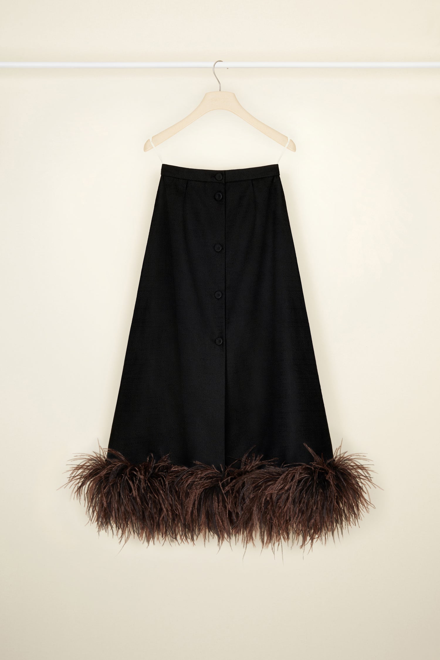 Patou - Jupe midi en tweed bio et plumes - Black - Léger comme une plume, on le porte partout : le tweed selon Patou.Jupe en tweed de coton et laine bio noir. Longueur midi. Boutons recouverts de tissus sur le devant. Poches latérales. Ourlet décoré de plumes d’autruche marron.