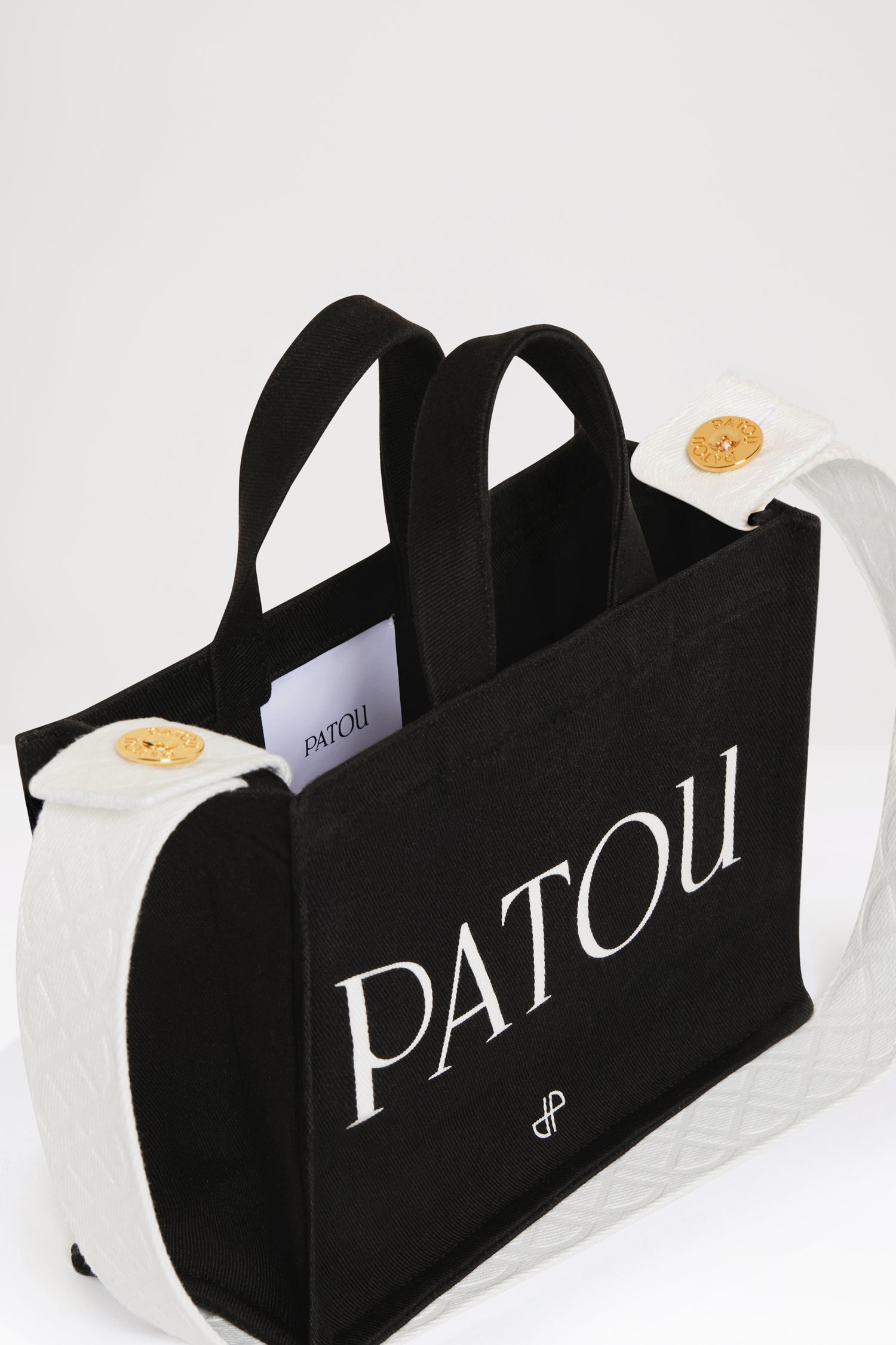 Patou - Petit cabas Patou en coton bio - Black - Le cabas Patou à emporter partout !Cabas en coton bio noir. Logo Patou et monogramme JP blancs. Bandoulière blanche à motifs JP en relief rattachée par deux boutons dorés. Double anse. Peut être porté à la main ou sur l&amp;#39;épaule.
