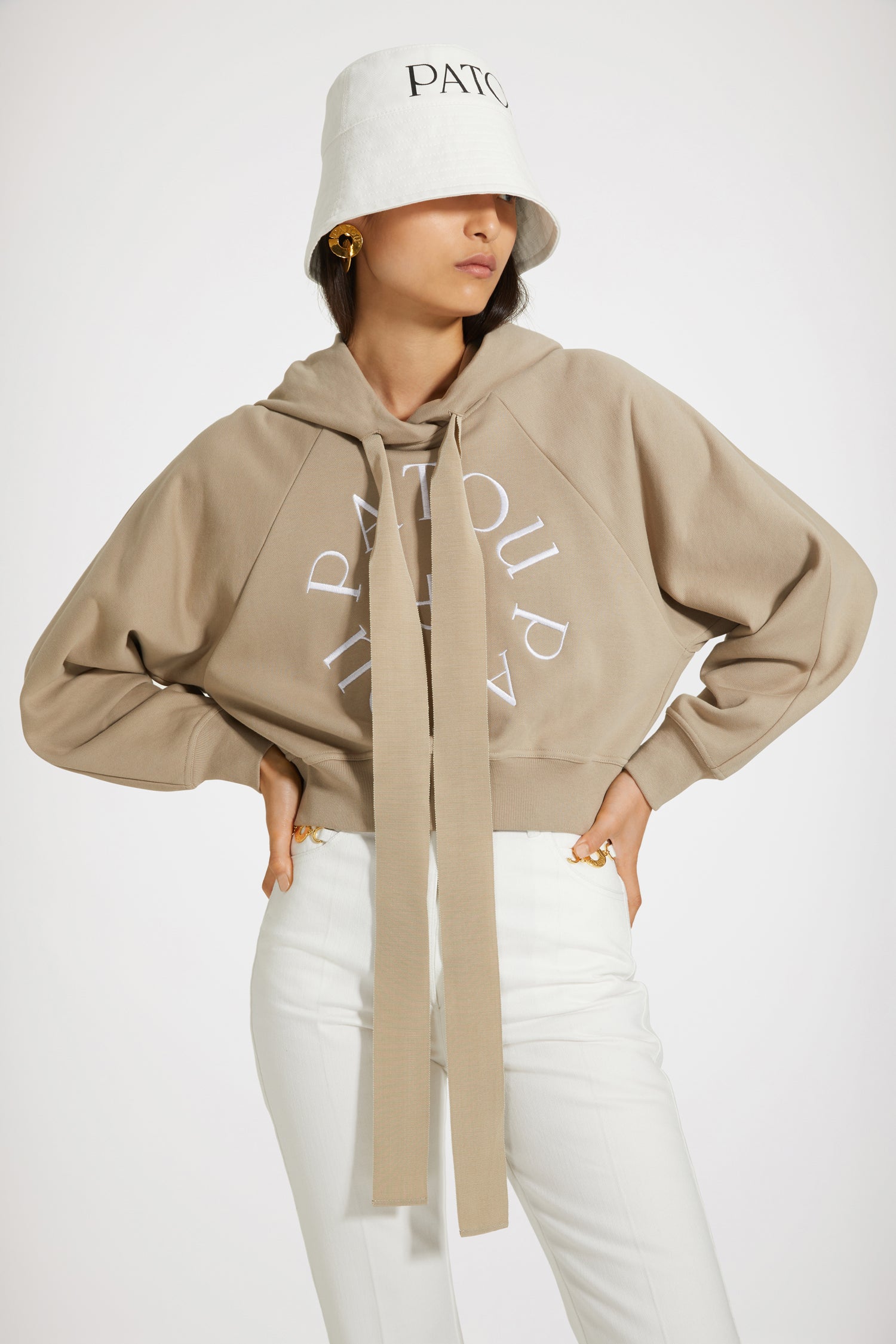 Patou - Felpa corta con logo medaglione in cotone bio - Parchment - Variazione di stagione sulla felpa Patou.Felpa in cotone bio beige pergamena. Modello corto. Collo con cappuccio e lacci in grosgrain. Logo Patou medaglione ricamato sul davanti. Maniche raglan. Polsini e vita a costine.