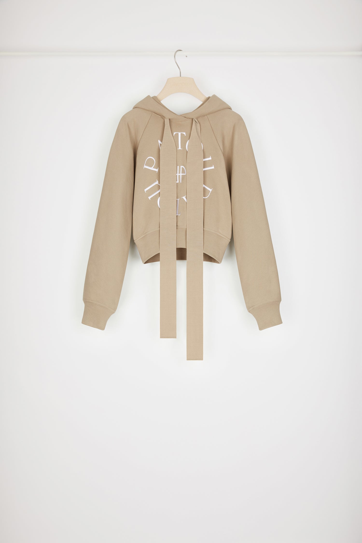 Patou - Felpa corta con logo medaglione in cotone bio - Parchment - Variazione di stagione sulla felpa Patou.Felpa in cotone bio beige pergamena. Modello corto. Collo con cappuccio e lacci in grosgrain. Logo Patou medaglione ricamato sul davanti. Maniche raglan. Polsini e vita a costine.