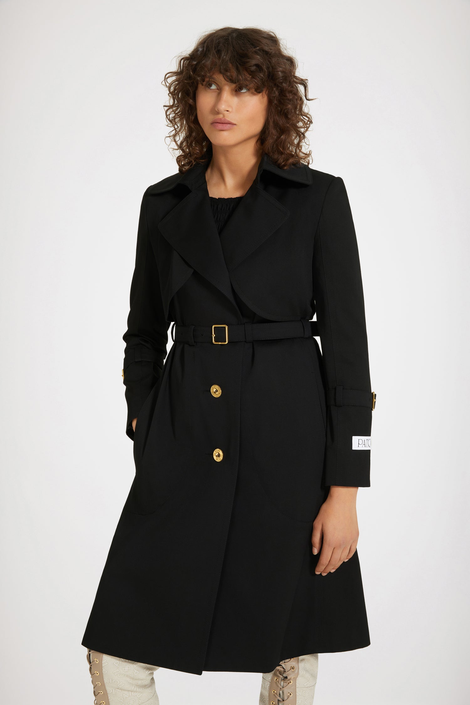 Patou - Trench coat in organic cotton gabardine - Black - How Patou fits and feels.Black organic cotton gabardine trench coat. Tailored single-breasted silhouette. Knee length. Notch lapels. Storm flap at the front. Gold-tone Patou-engraved buttons at the front. Adjustable gold-tone buckle belt that sits at the waist. Side seam patch pockets at the front. Belted cuffs. Signature Patou label on the left arm. Signature curved seam at the back. Single back vent with gold-tone Patou-engraved button.