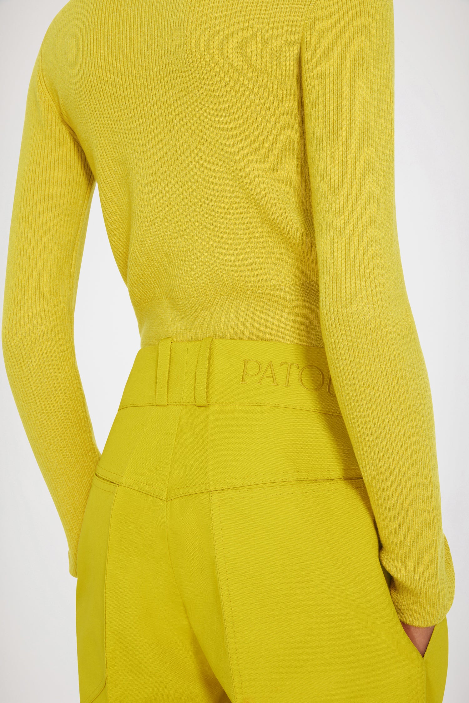 Patou - Flared trousers in organic cotton - Absinthe - Low rise, high craftsmanship: the perfect Patou trousers. Absinthe yellow organic cotton canvas trousers. Slightly flared straight leg with crease at the front and back. Low rise. Gold-tone Patou engraved button fastening at the front. Belt loops. Patou logo embroidered at the back. Pockets at the sides. Wide pockets at the back to complement the Eiffel tower construction.