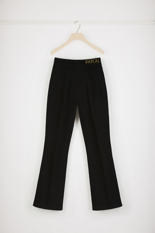 Patou - オーガニックコットンデニム製 フレアーパンツ - Black - ジャン・パトゥのアートが昇華された新しいパトゥデニム。ブラックカラーのオーガニックコットンデニム製パンツ。フレアーカット。ミッドライズ。フロントにゴールドトーンのパトゥ刻印入りボタン。ベルトループ付き。ウエストバンドにパトゥの刺しゅうロゴ。フロントとバックにダーツ使いとセンター位置の折り目。フロントにゴールドカラーのJP刻印入りオーナメントをあしらったポケット2つ。バックにブランドを象徴するカーブシーム。The ornament can be removed.
